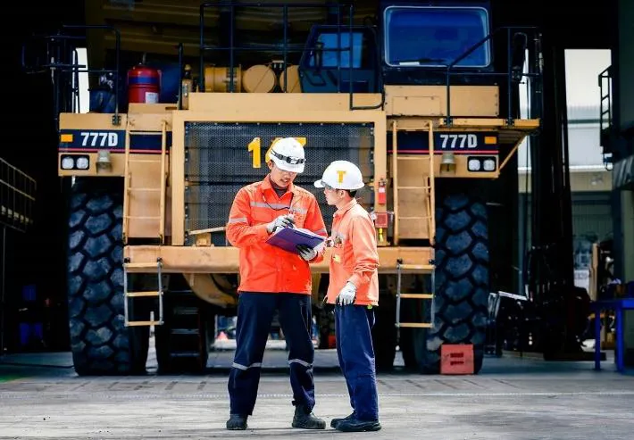 Two mine workers reviewing a checklist in front of a CAT 777D haul truck