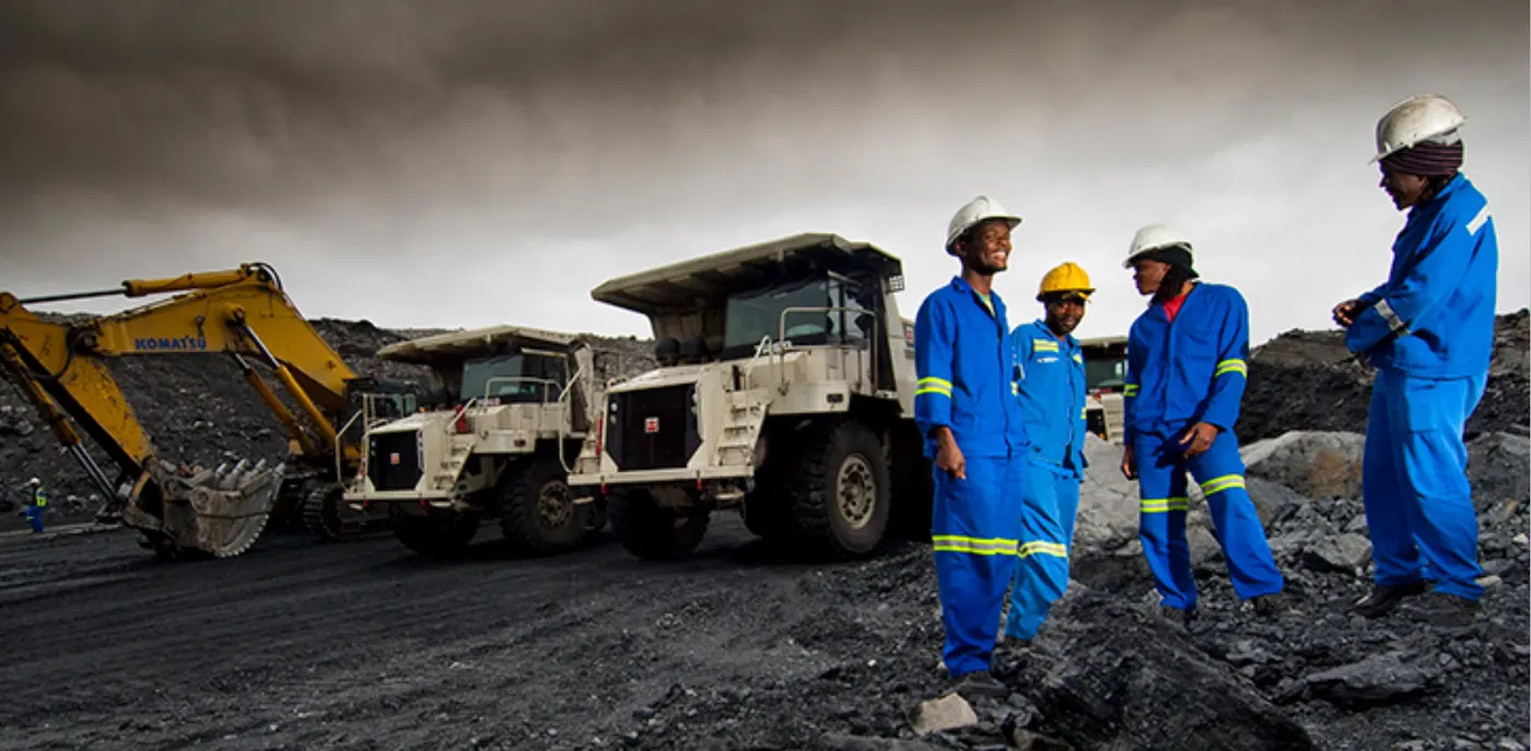 Mine crew in safety gear beside an excavator and haul trucks